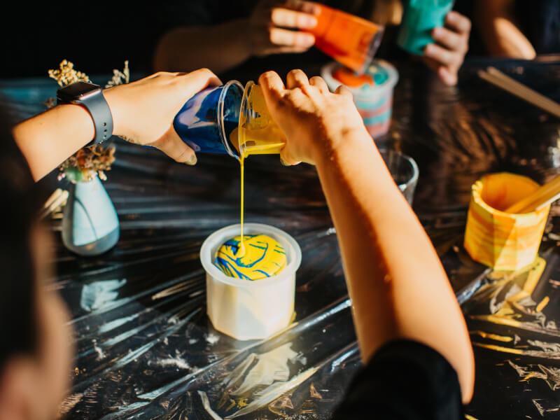 Someone pouring two brightly coloured resins to make a pot in a Manchester craft class.
